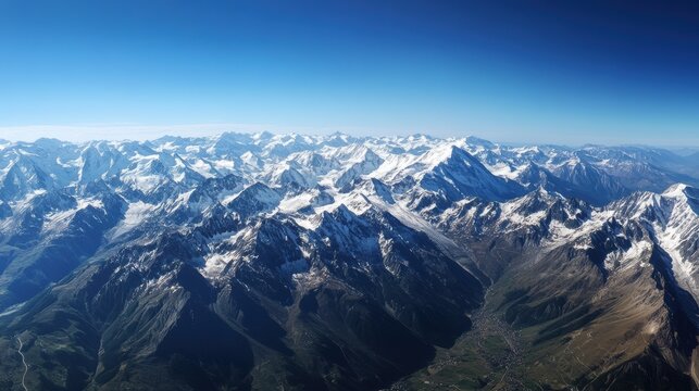 Aerial view of snow-capped mountain range under a clear blue sky, showcasing the rugged terrain and vastness of nature.