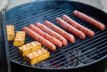 Sausages and grilled tofu sizzle on the barbecue, perfect for a sunny day celebration with friends