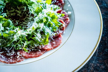 A beautifully arranged plate featuring thinly sliced carpaccio, topped with fresh greens and cheese