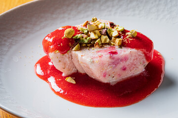 A creamy panna cotta rests elegantly on a bed of rich berry sauce, adorned with crunchy pistachios