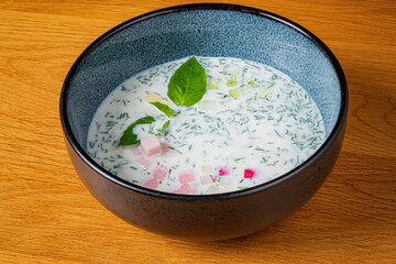 A bowl filled with chilled soup featuring fresh herbs, diced vegetables, and a splash of color