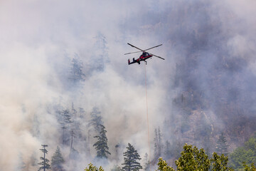 Helicopter Fighting Forest Fire in Smoky Mountainous Terrain Amid Dense Fog