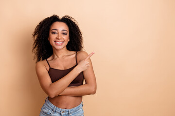 Confident young woman standing against beige background pointing with a smile wearing stylish...