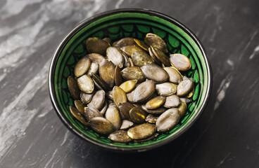 Pumpkin seeds in ceramic bowl. Close-up of roasted snack on marble surface. Natural healthy superfood full of fiber and minerals. Rustic diet ingredient for salads and fitness recipes.