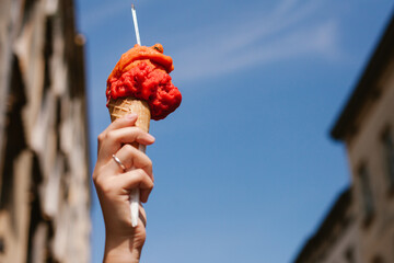 Woman holding delicious red ice cream in cone against blue sky in italian city