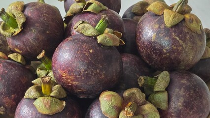 Stacked fresh mangosteens with purple outer skin and green sepals in natural light, ideal for...