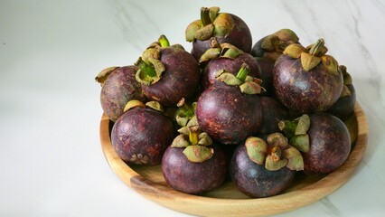 Mangosteens arranged on a round wooden plate, photographed in daylight with white marble countertop background.