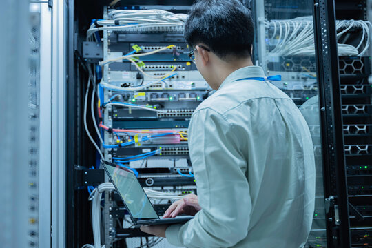 Computer engineer is setting up network in server room,Systems Maintenance Technician,Male engineer working in server room at modern data center - Powered by Adobe