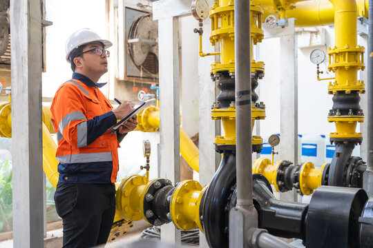 Asian engineer wearing glasses working in the boiler room,maintenance checking technical data of heating system equipment,Thailand people