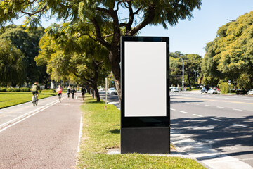 A vertical blank billboard on the street next to a park with running trails. Copy space poster on a...