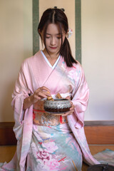 Vertical young Japanese woman in traditional kimono or yukata clothing making traditional tea