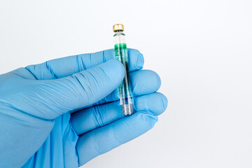 Gloved Hand Holding Medical Vaccine Vial on White Background, Dental Anesthesia Syringe.Close-up of a blue-gloved hand holding a small glass vaccine vial with a green label