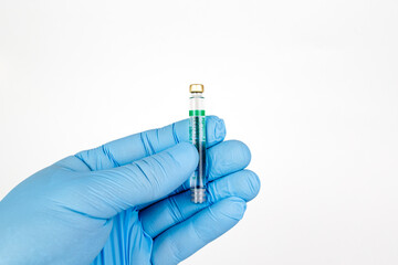 Gloved Hand Holding Medical Vaccine Vial on White Background, Dental Anesthesia Syringe.Close-up of a blue-gloved hand holding a small glass vaccine vial with a green label