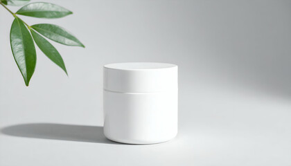 White cosmetic jar next to green leaves on a light background.