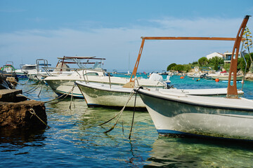 Motor boats moored to stone pier in sea water with coastal houses in background. Calm sea bay with...