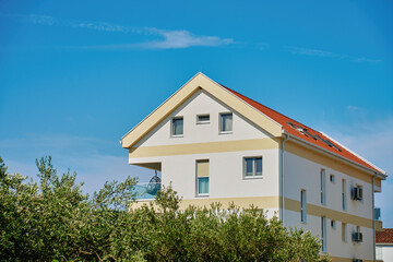 Modern white house facade with windows, balcony and garden. Contemporary residential architecture under blue sky