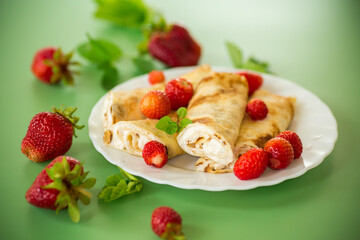 Plate with pancakes and fresh strawberries on a green background