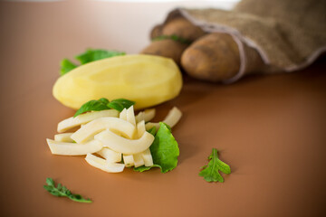 Raw peeled potatoes and slices on a brown background