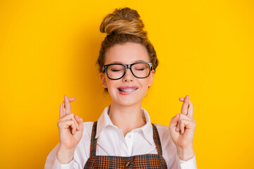 Smiling young lady with crossed fingers hoping for success, wearing glasses and stylish uniform,...