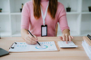 Young businesswoman calculating and analyzing financial data using calculator and computer while working on charts and graphs in modern office