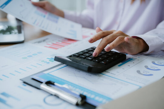 Businesswoman analyzing financial charts and using calculator in office