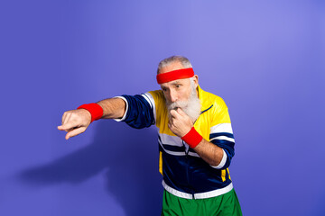 Energetic elderly man in colorful retro sportswear, playfully blowing whistle and posing against...