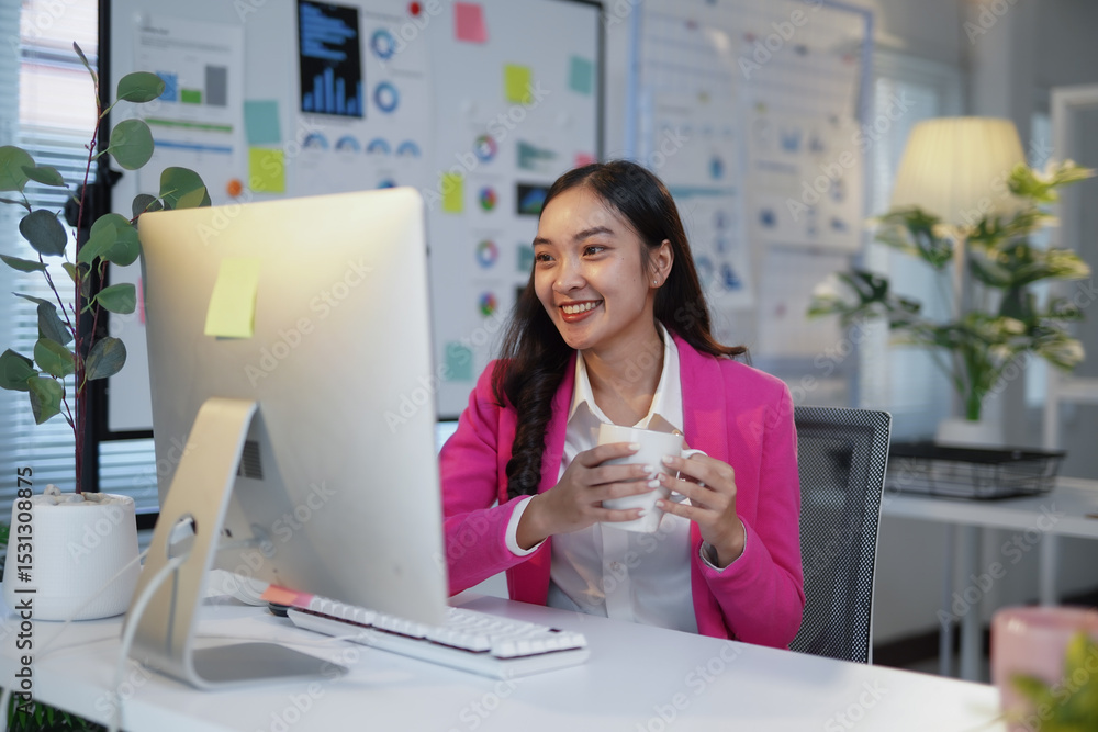 Poster young asian manager enjoying a coffee break while working on a desktop computer in a bright and mode