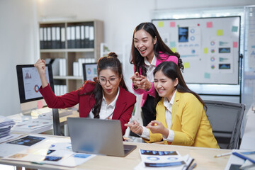 Group of asian businesswomen expressing excitement and joy after achieving successful results on a project, looking at laptop screen in modern office