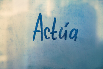 Spanish message word Actua is Act in English on foggy glass on blue window