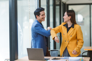 Asian businesspeople wearing smart casual bumping elbows to avoid spreading germs in the office