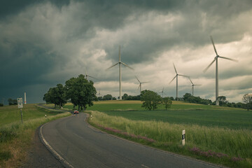 Wind turbines, nestled amidst the countryside, stand tall under the dark, rainy sky.