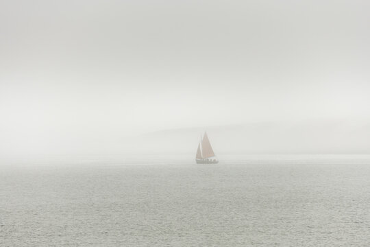 A sailboat is sailing in the ocean on a foggy day