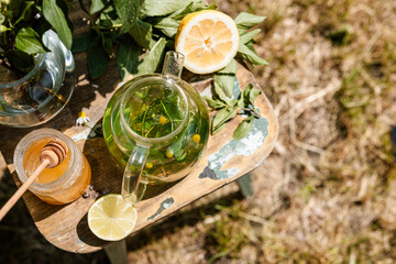 Hot herbal tea in a glass teapot steaming gently in the summer garden top view. Honey and lime suggest a healthy sugar-free tea ritual in a cozy outdoor setting.