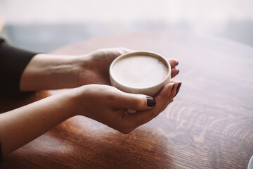 Warm hands delicately cradle a cup of coffee over a beautifully textured wooden surface.