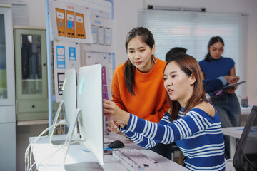 Two young women, probably web designers, collaborating on a project in a contemporary office, focusing on a desktop computer display