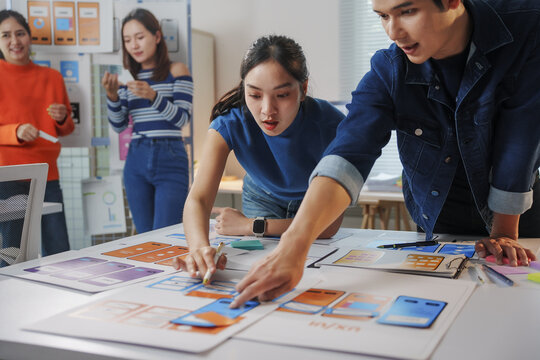 Young Asian ux designers reviewing mobile app interface wireframe in the office, working together on design project