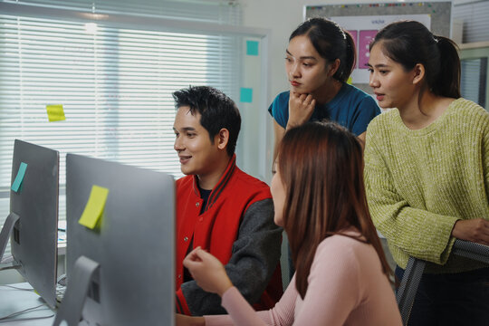 Group of young Southeast Asian web developers collaborating on a project, looking at computer screen and discussing code in a modern office