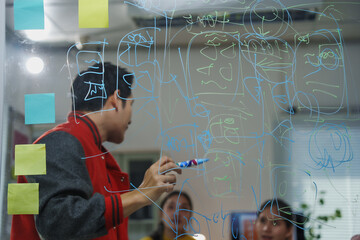 Developer drawing software design scheme on transparent board with sticky notes in office,...