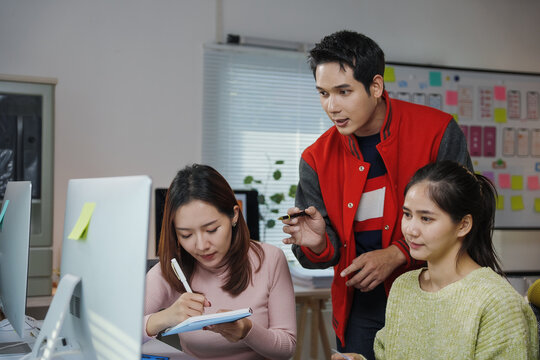 Asian manager explaining project details to young employees working on desktop computer in the office