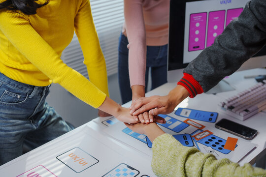 Four uxui designers joining hands over a table, showing teamwork and collaboration in a software development office