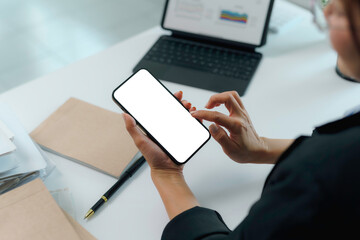 Businesswoman holding a smartphone with a blank screen, analyzing marketing data while working at her modern office desk