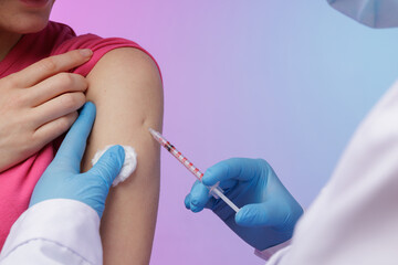 Close-up of a healthcare worker administering a vaccine injection into a patient’s upper arm,...