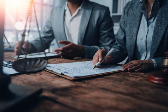 Lawyers are discussing contract details during a meeting in a law office, with legal documents and scales of justice on the table