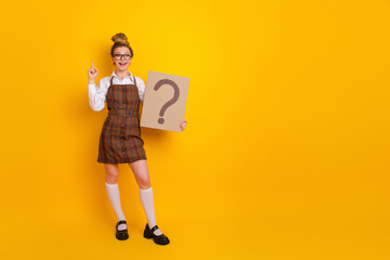 Young student in stylish plaid school uniform holding a question card and pointing up on a vibrant...