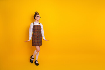 Teen girl female student in stylish academic outfit posing against vibrant yellow backdrop,...