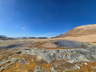 Experience a stunning Hverir geothermal landscape in Iceland featuring bubbling hot springs surrounded by unique rocky terrain. A clear blue sky enhances the natural beauty of this environment.