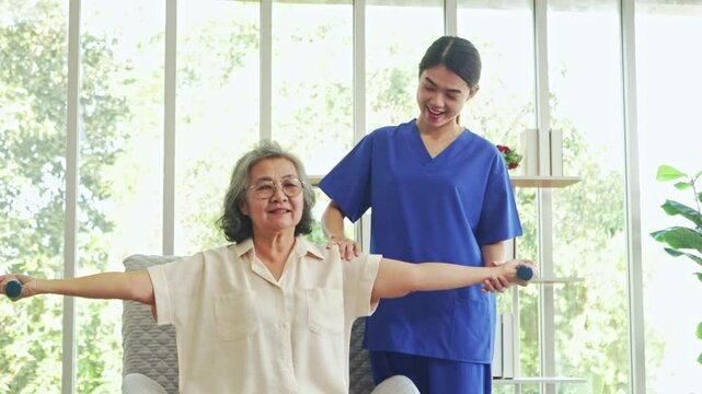 Female physiotherapist is providing nursing care an elderly female patient with muscular dystrophy training her to do dumbbell exercises rehabilitate her muscles and prevent beriberi.