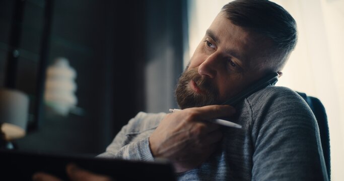 Close Up of Financial Analyst Talking on Phone, Working on Tablet Computer, Monitoring Real-Time Stocks, Exchange Market Charts. Successful Businessman Works in Comfortable Office of Investment Bank.