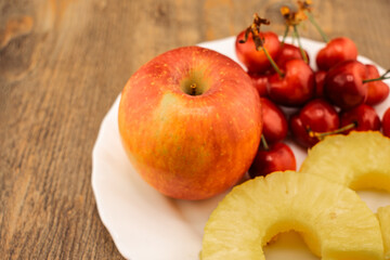 pineapple rings, red cherries, and a red and yellow apple are artfully arranged, healthy and appealing produce. Ideal for themes of wholesome eating, summer refreshments, and natural food beauty
