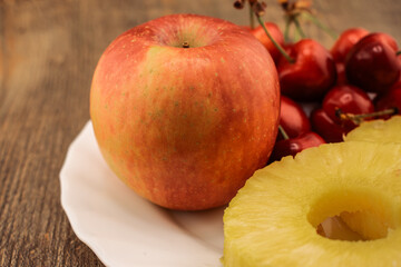 pineapple rings, red cherries, and a red and yellow apple are artfully arranged, healthy and...
